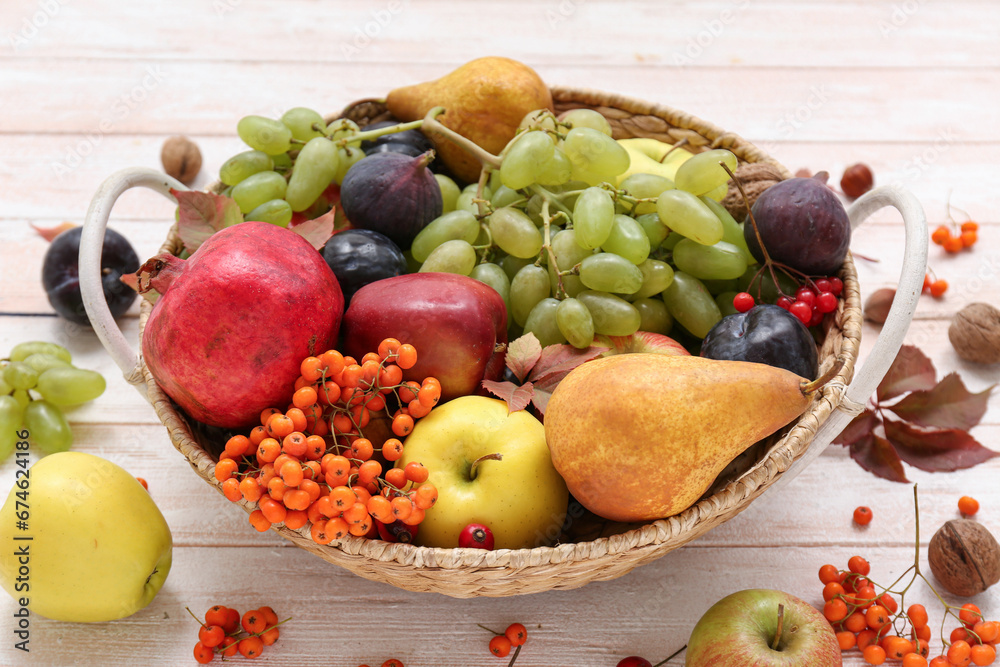 Wicker basket with different fresh fruits on white wooden background