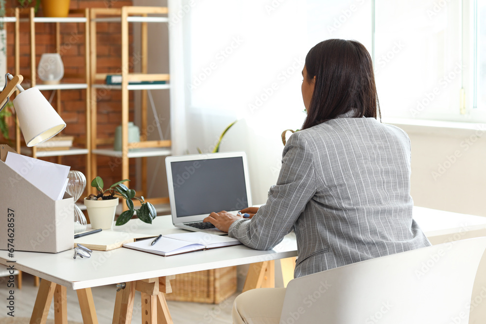 Young woman working with laptop at home office, back view