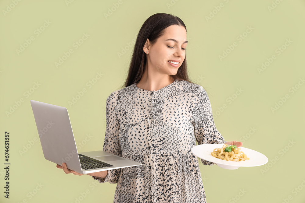 Young woman with tasty pasta and laptop on green background