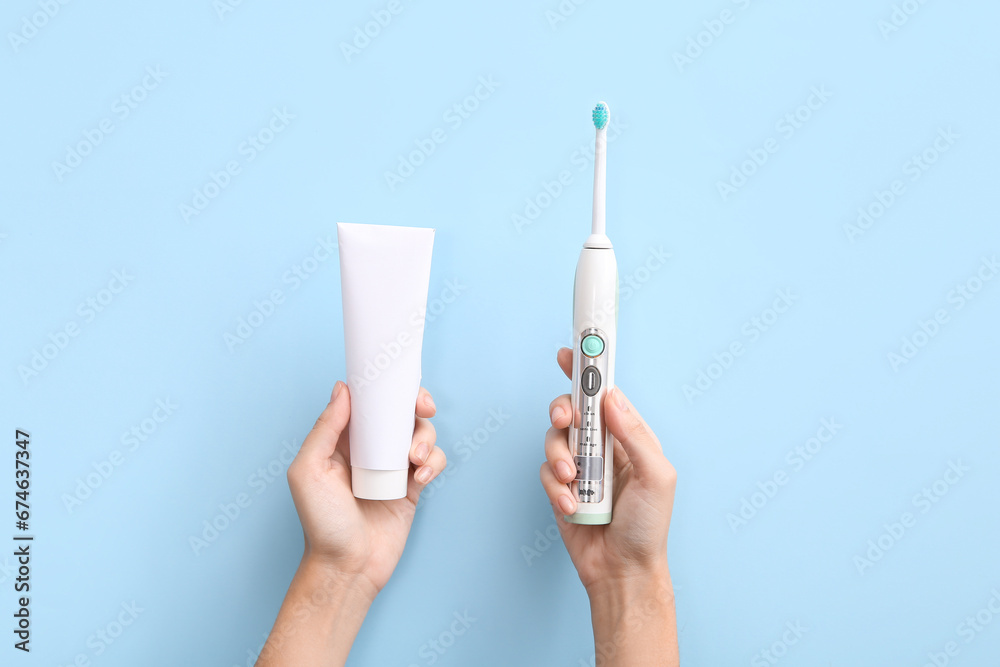 Female hands with electric toothbrush and toothpaste on blue background.