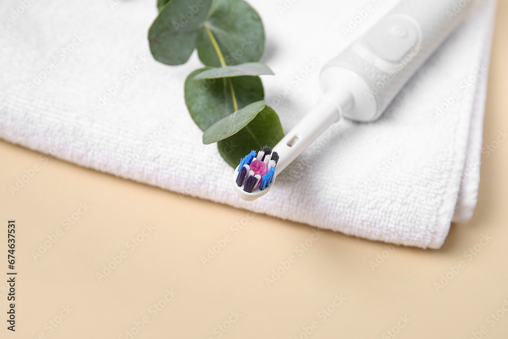 Electric toothbrush with eucalyptus branch and towel on color background.