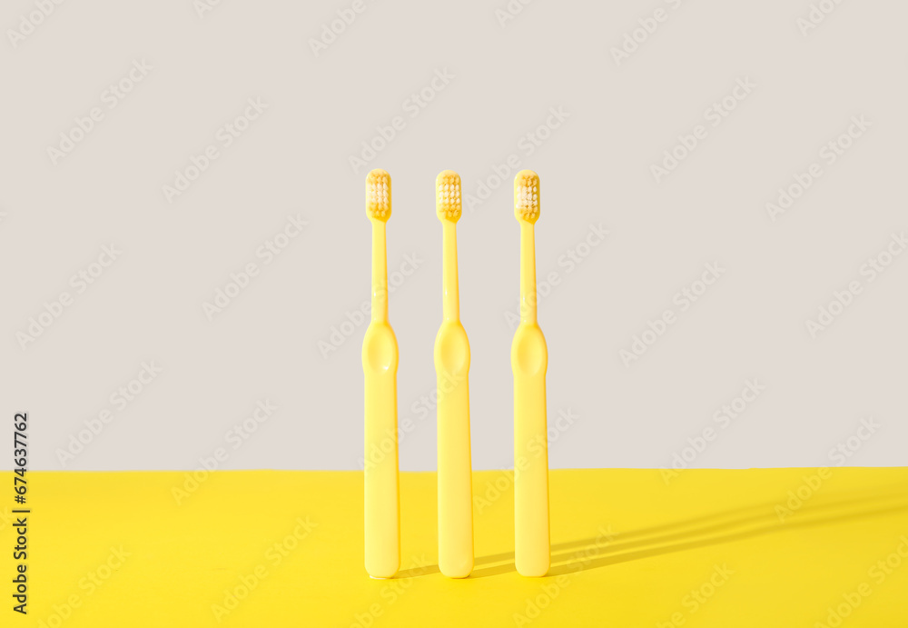 Three yellow toothbrushes on color background.