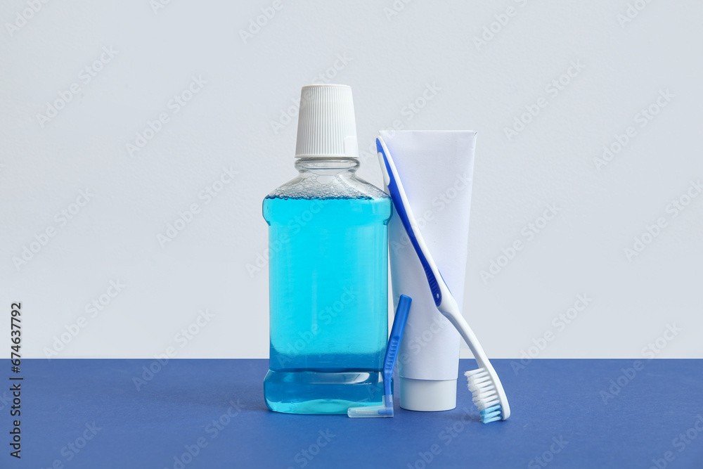 Mouth rinse with toothbrush and toothpaste on color background.