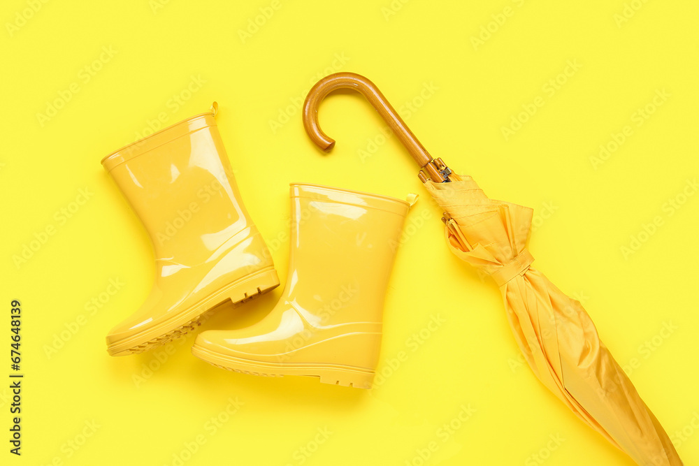 Yellow stylish umbrella and gumboots on color background