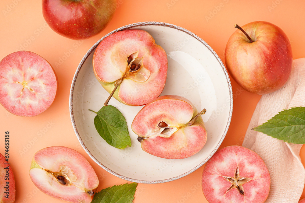 Plate with halves of sweet pink apple and leaves on orange background