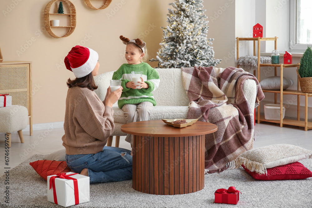 Young mother and her little daughter drinking milk at home on Christmas eve