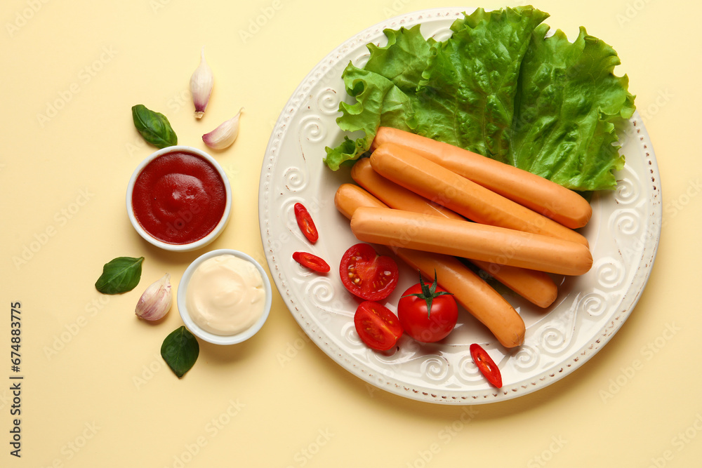 Plate of tasty sausages with lettuce and tomatoes on beige background