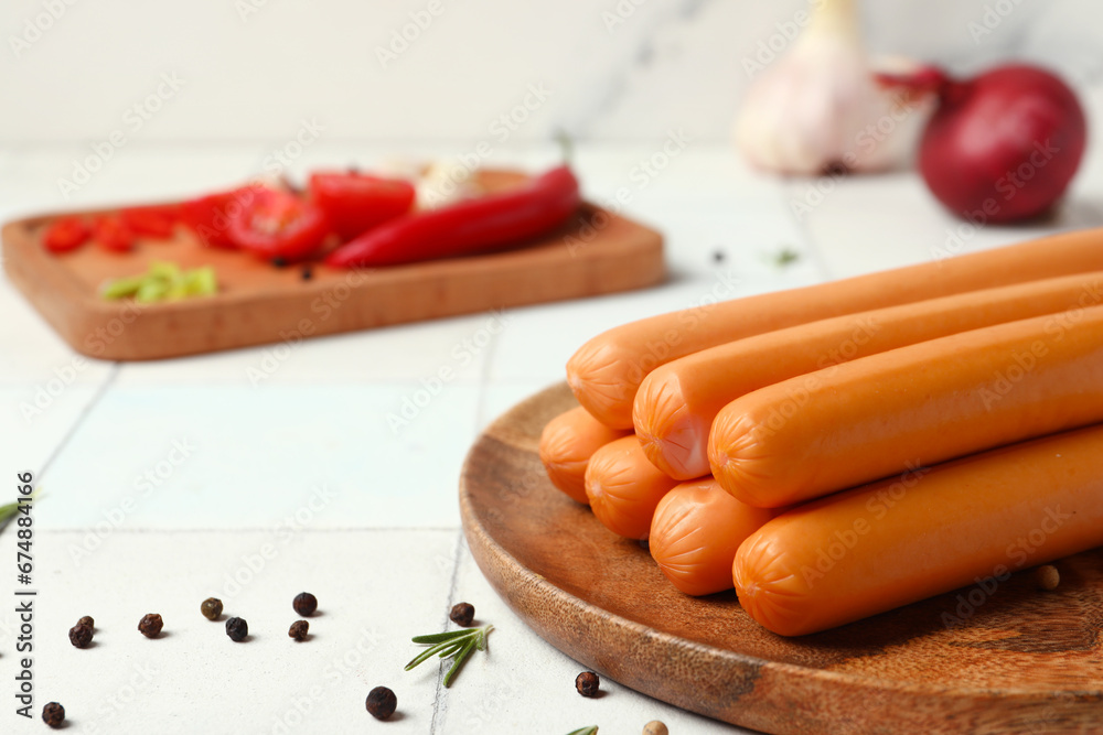 Board and plate of tasty sausages with tomatoes on white tile background