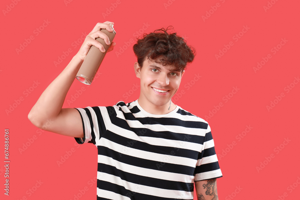 Handsome young man applying hair spray on his curly hair against red background