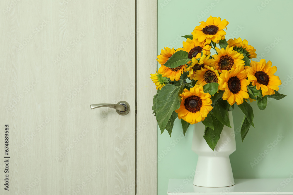 Vase with beautiful sunflowers on white table near green wall