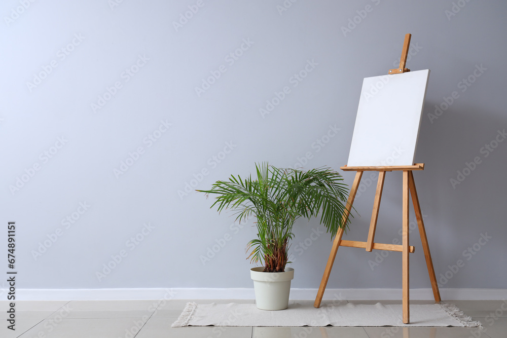 Wooden easel with blank canvas near grey wall