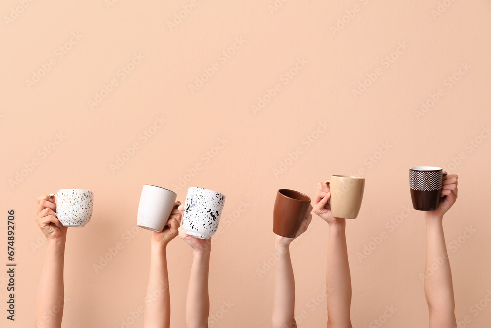 Women holding cups of hot coffee on beige background