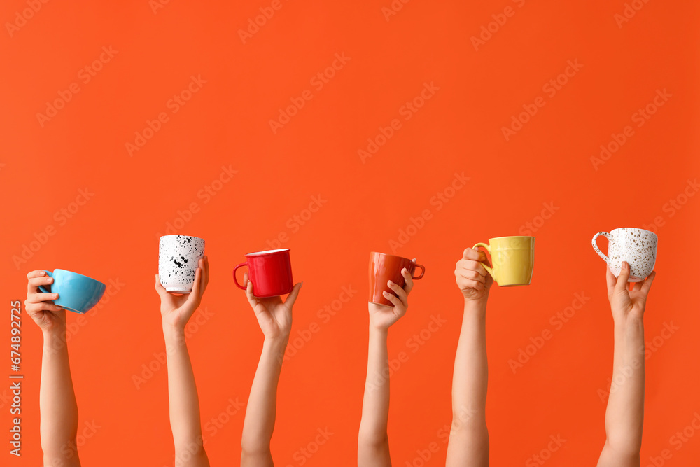 Women holding cups of hot coffee on orange background