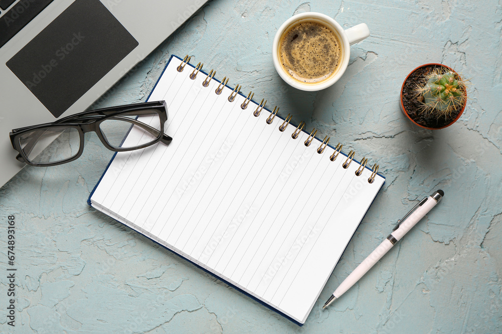 Notebook with eyeglasses and cup of tasty coffee on blue background