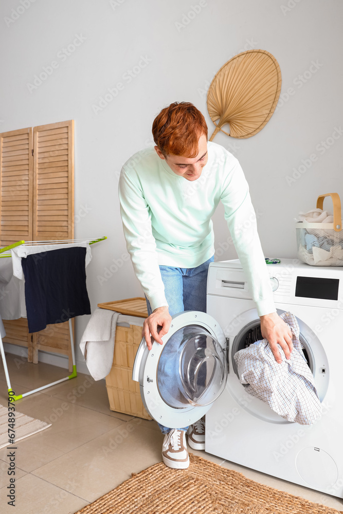 Young man putting laundry into washing machine at home