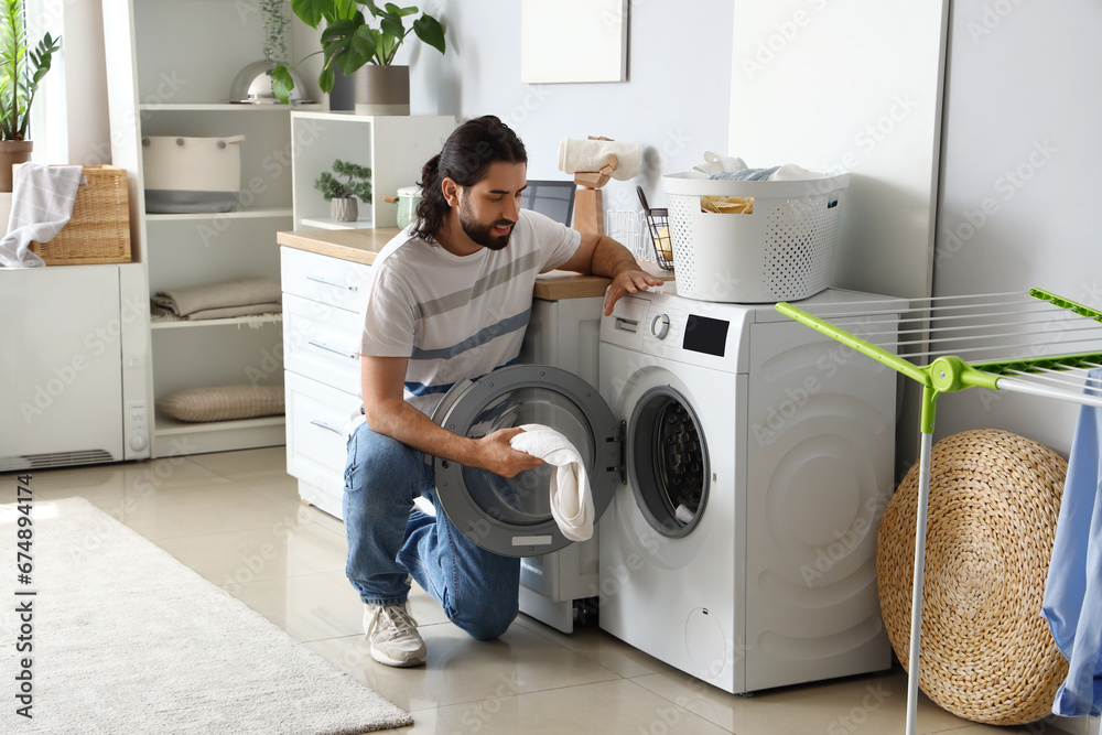 Young man putting laundry into washing machine at home