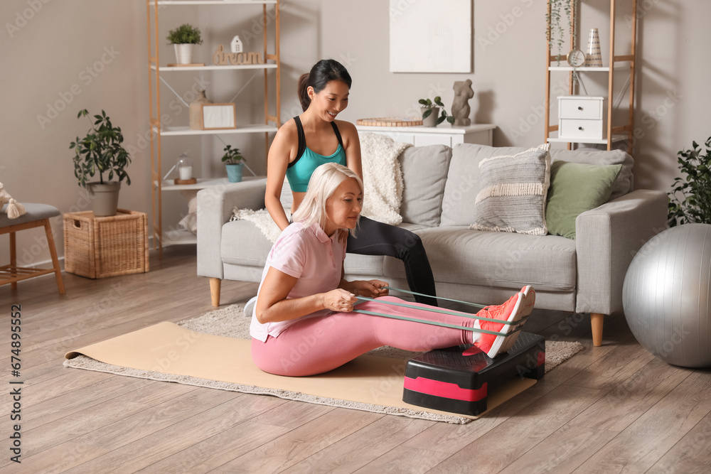 Mature woman training on mat with rehabilitation therapist at home