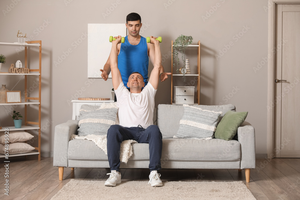 Mature man training with dumbbells and rehabilitation therapist at home