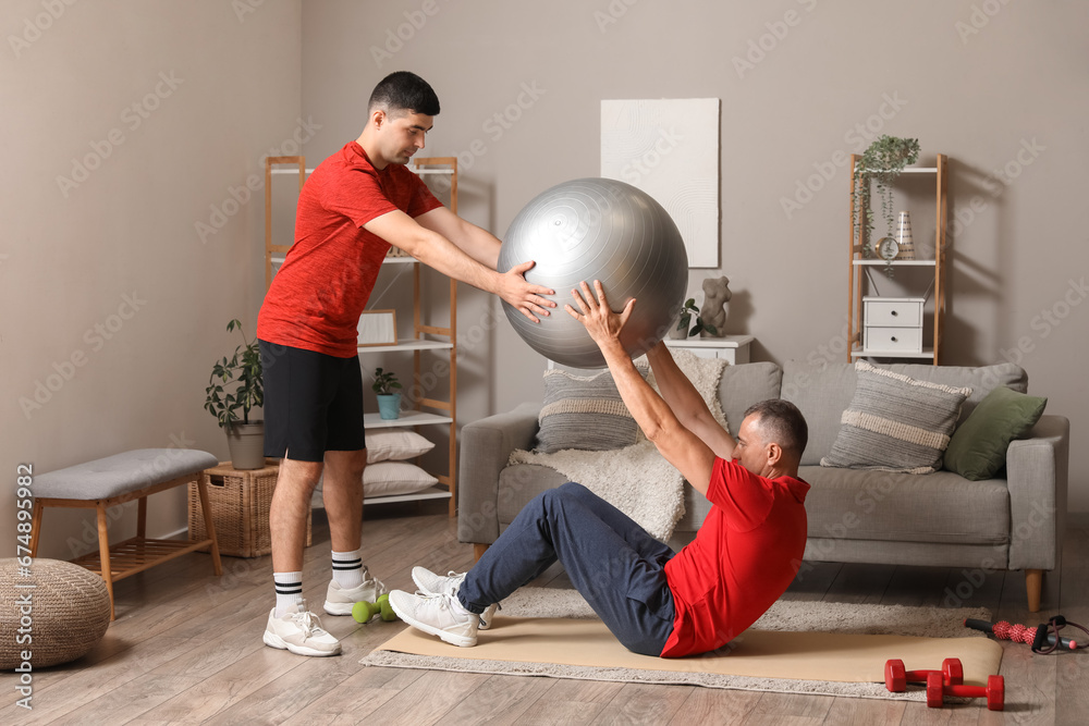 Mature man training with fitball and rehabilitation therapist at home