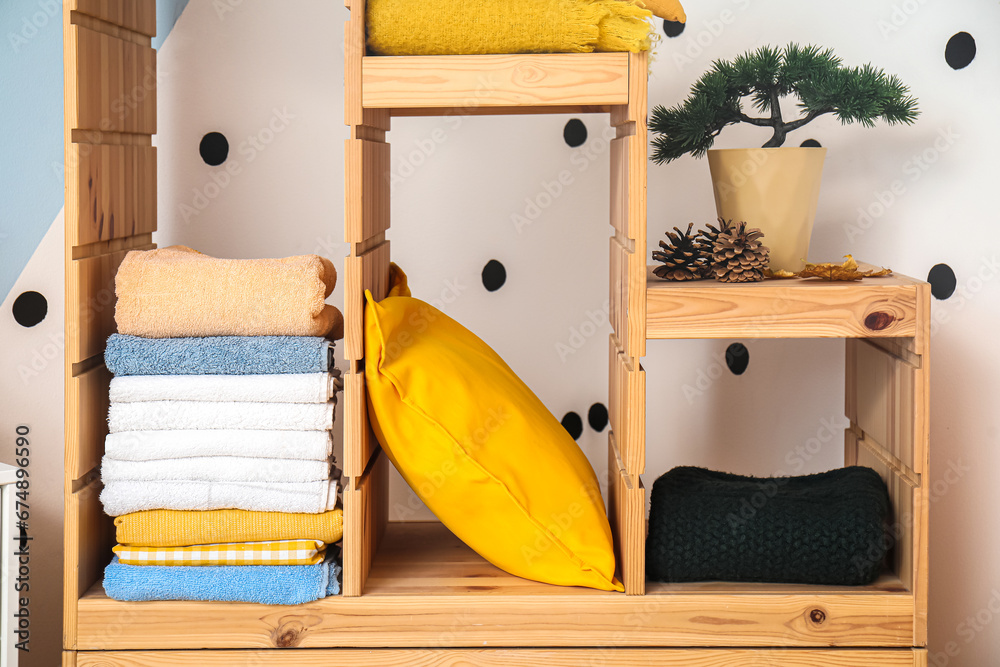 Wooden shelving unit with clean towels, pillow and decor in room