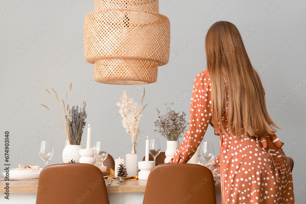 Beautiful woman setting table with dried flowers in dining room