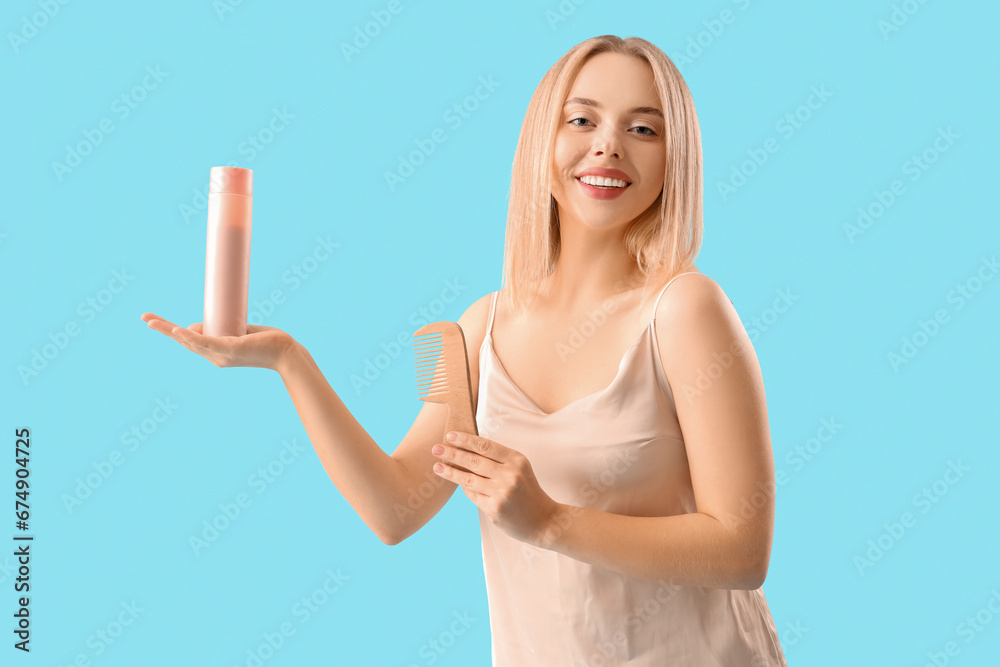 Young blonde woman with bottle of hair product on blue background