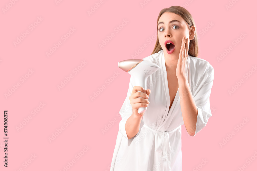 Beautiful shocked woman with modern photoepilator on pink background