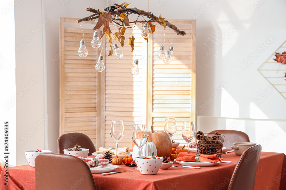 Autumn table setting with pumpkins and pine cones in light dining room