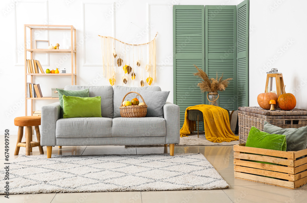 Interior of living room with grey sofa, autumn leaves and pumpkins in wicker basket