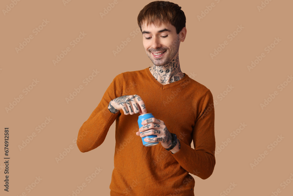 Happy young man opening can of soda on brown background