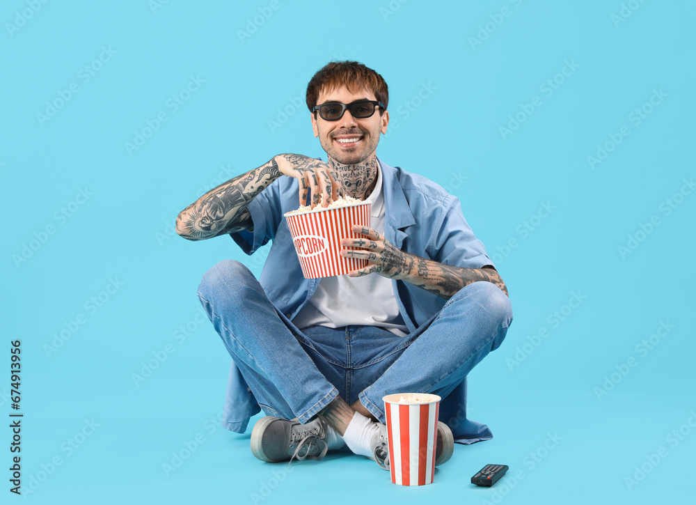 Happy young man with popcorn and TV remote watching movie on blue background