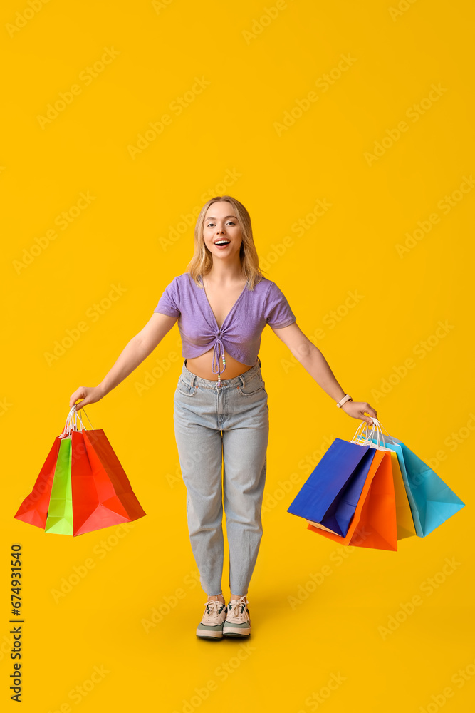 Young woman with shopping bags on yellow background