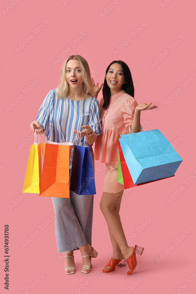 Beautiful young women with shopping bags on pink background