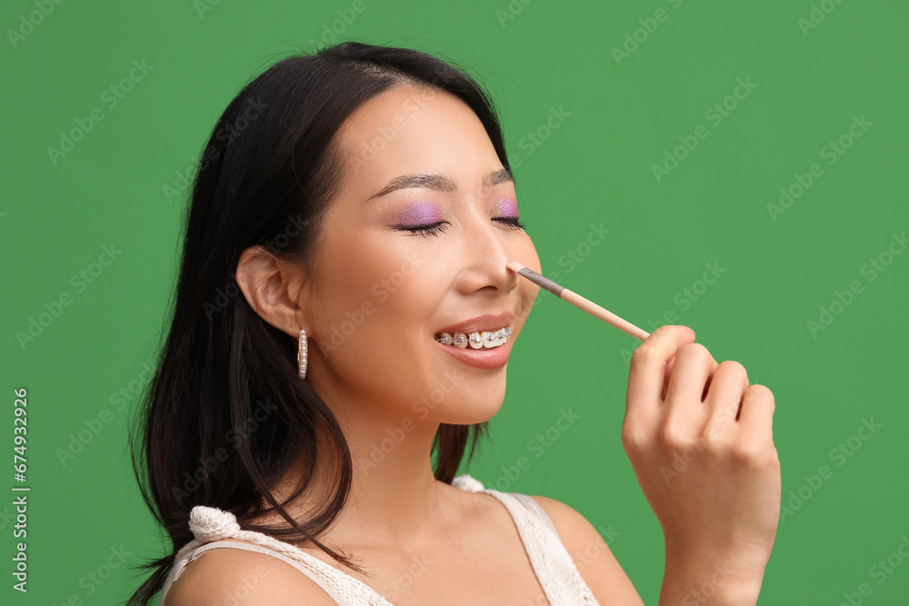 Young Asian woman with makeup brush on green background