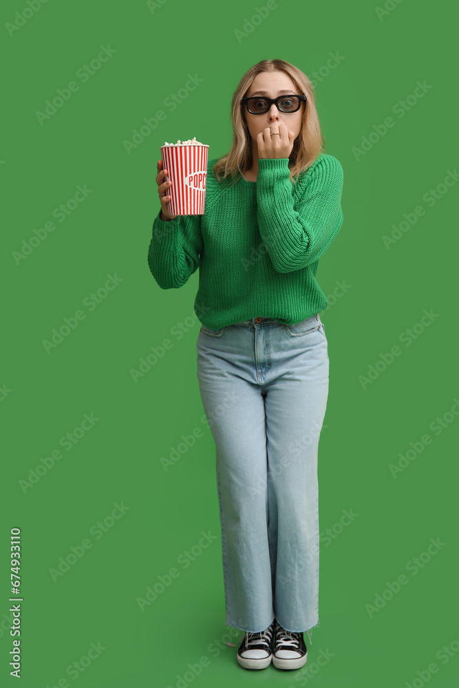 Young woman in 3D glasses with bucket of popcorn on green background