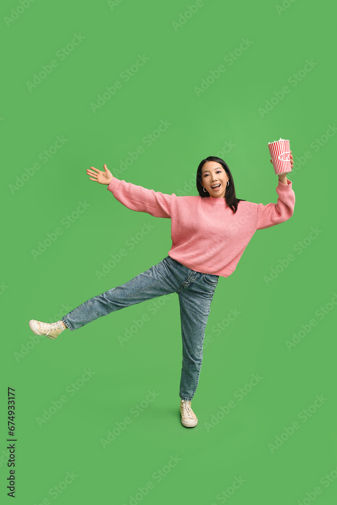 Young Asian woman with bucket of popcorn on green background