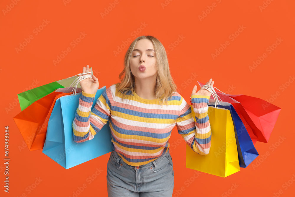 Young woman with shopping bags on orange background