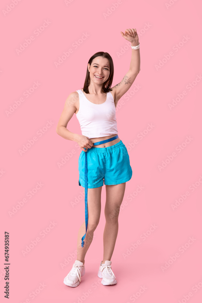 Beautiful young sporty woman with measuring tape on pink background. Weight loss concept