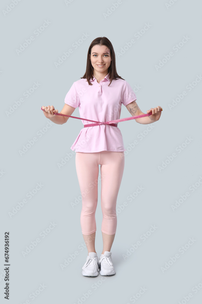 Beautiful young sporty woman with measuring tape on grey background. Weight loss concept