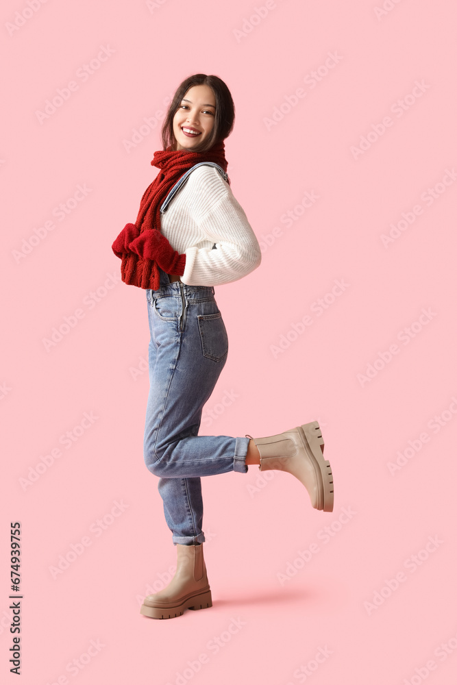 Beautiful young Asian woman in warm scarf and gloves on pink background