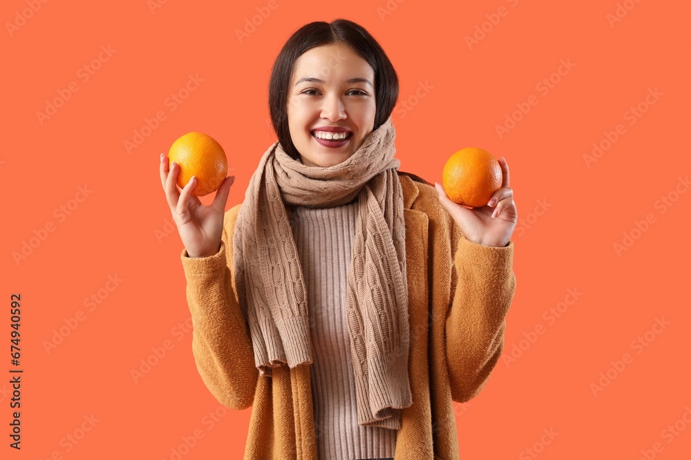 Beautiful young Asian woman in warm scarf with oranges on color background