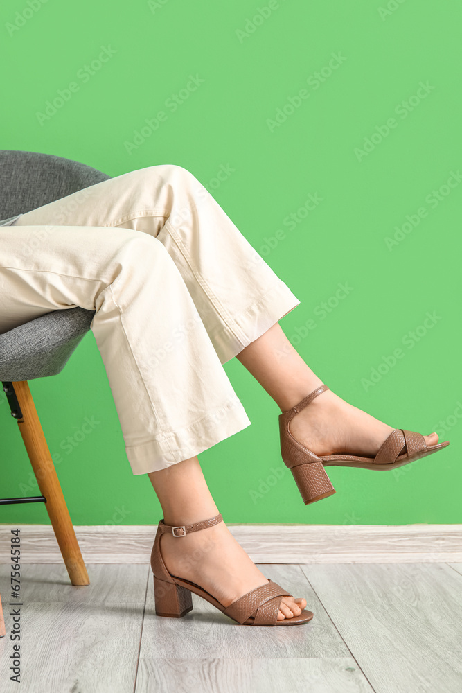 Woman in stylish shoes sitting on armchair near color wall