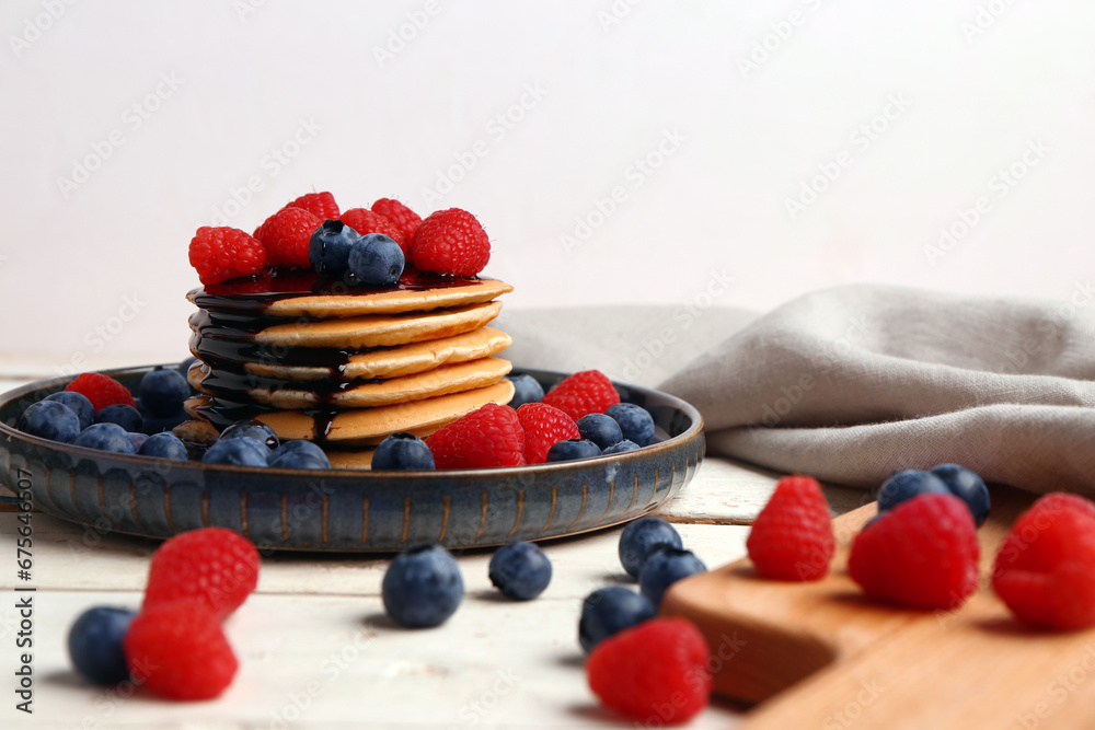 Plate with sweet pancakes and berries on light wooden background, closeup