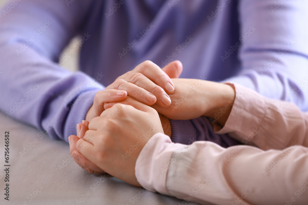 Young woman and her grandmother holding hands at table in kitchen, closeup