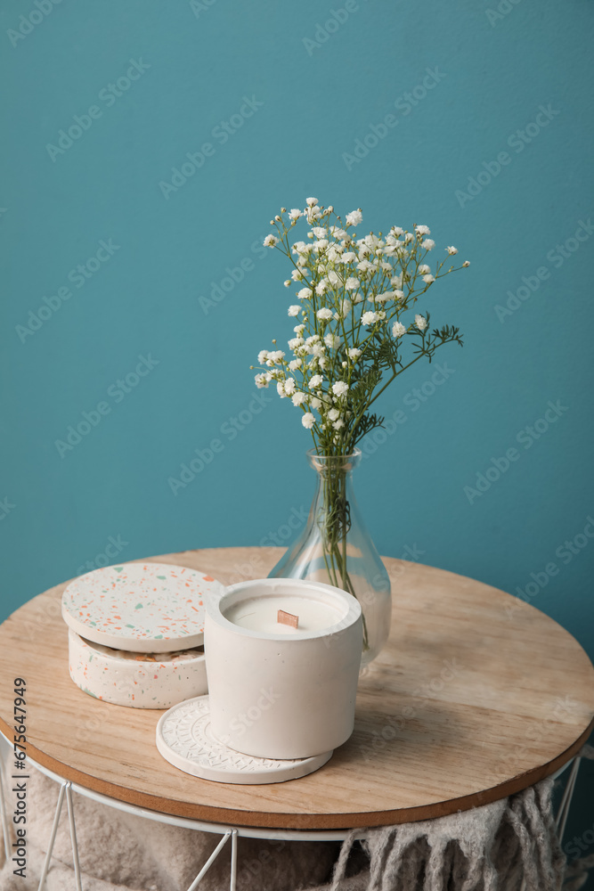 Gypsophila flowers and candle on table near turquoise wall in room, closeup