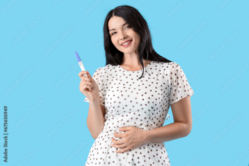 Portrait of happy young woman with pregnancy test on blue background