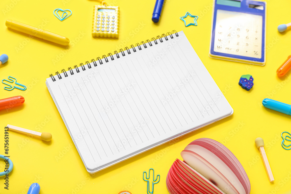 Notebook with different stationery supplies on yellow background