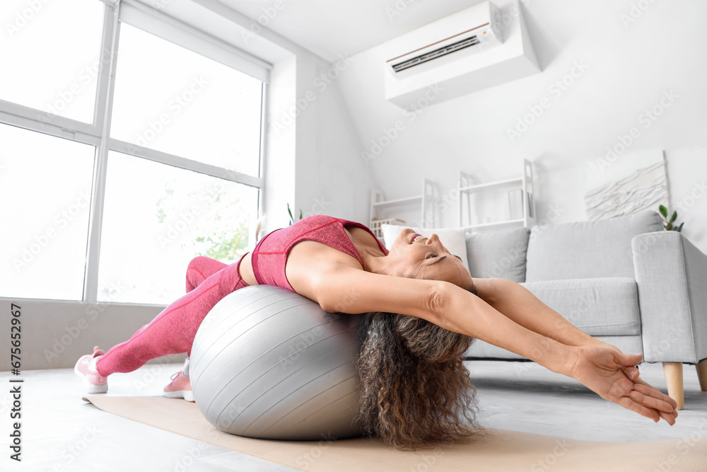 Beautiful adult woman exercising on fitness ball at home