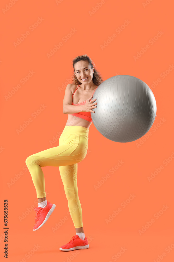 Beautiful adult woman in sportswear with fitness ball on orange background