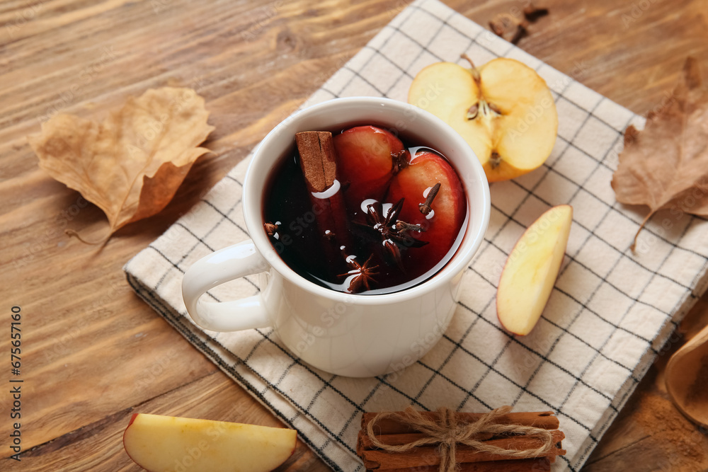 Cup of hot mulled wine with apple and cinnamon on wooden background